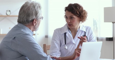 Wall Mural - Senior adult male patient listening medical prescription handshaking thanking female doctor for good treatment result. Lady physician shaking hand of old elder client after healthcare checkup meeting.