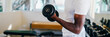 © twinsterphoto - Young African American man standing and lifting a dumbbell with the rack at gym. Male weight training person doing a biceps curl in fitness center