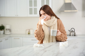 Poster - Sick young woman with cup of hot drink and tissues in kitchen. Influenza virus