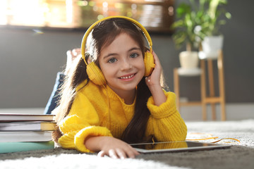 Sticker - Cute little girl with headphones and tablet listening to audiobook at home