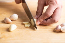 Hand Holding Kitchen Knife And Chopping Garlic On Wooden Board For Cooking