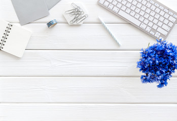 Poster - Spring inspiration concept. Work desk with cornflowers bouquet on white wooden background top-down frame copy space