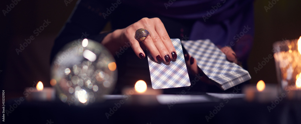 Close-up of fortuneteller's hands with cards at table with candles, magic ball in dark room - obrazy, fototapety, plakaty 