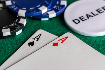 A close-up of a pair of aces, diamonds and spades, on standard playing cards.  on a green felt surface with black and blue betting chips and a dealer chip.  Room for copy