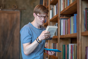 Young man in eyewear reading the title of the book