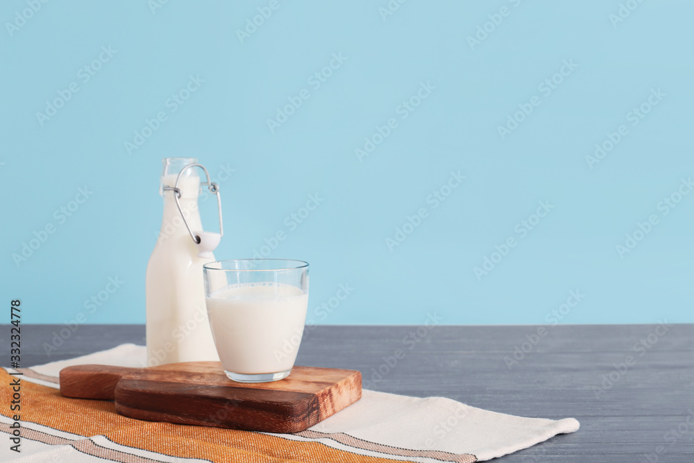 Glassware with fresh milk on table against color background