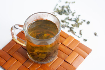 Сup with green tea brewed in it on a wooden stand for hot tea and scattered dry leaves tea on a white background