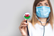 female doctor in a medical mask holds a stethoscope on a light background. Added flag of Wales. Concept medicine, level of medicine, virus, epidemic