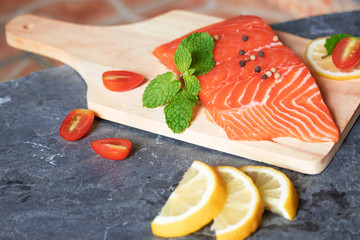 Salmon. Fresh raw salmon fish. Raw salmon fillet with pepper, herbs, lemon, tomato ingredients for cooking on black stone table rustic style. Top view with copy space.