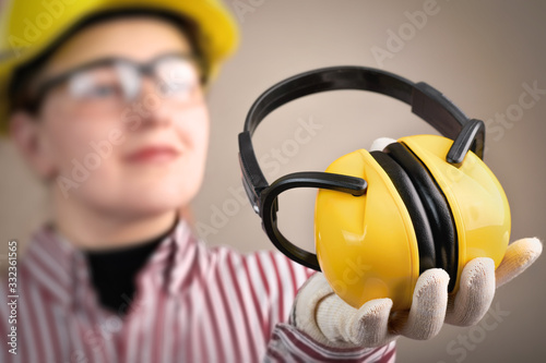 Young woman in safety glasses and helmet holds earphones in her hand for hearing protection: safety and health at work concept and protective equipment