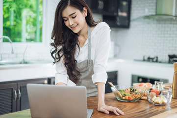 Image of young lady standing in kitchen using tablet computer and cooking vegetable salad with the tomatoes and avocado.