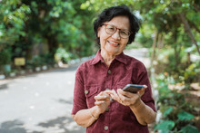 Smiling Asian Old Woman Using A Cell Phone When Looking To The Camera