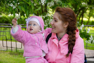 mom sits on the grass in the shade of a blossoming apple tree. plays and hugs his daughters