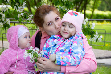 mom sits on the grass in the shade of a blossoming apple tree. plays and hugs his daughters