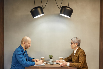 Wall Mural - Minimal side view portrait of mature bald man writing on clipboard while discussing contract with business manager during meeting at cafe table, copy space