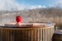 Young Adult Relaxing In Wooden Hot Tub Outside And Looking At Nature. Person Enjoying Hot Steaming Pool On A Sunny Day, Private Spa Treatment