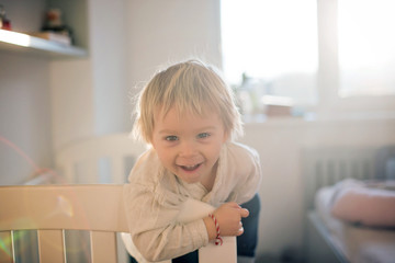 Sticker - Beautiful toddler blond boy, playing in children bed, beautiful light