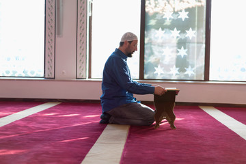 Wall Mural - Young Arabic Muslim man reading Koran and praying. Religious muslim man reading holy koran inside the mosque.