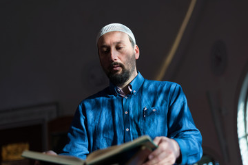 Wall Mural - Young Arabic Muslim man reading Koran and praying. Religious muslim man reading holy koran inside the mosque.