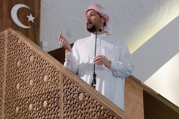 Wall Mural - Muslims young arabic Imam has a speech on friday afternoon prayer in mosque. Muslims have gathered for the friday afternoon prayer in mosque and are listening to the speech of imam