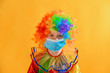 © andov - Sad and sad baby clown in a protective medical mask from coronavirus on a yellow background.
