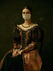 Medieval young woman as a duchess wearing protective mask against coronavirus spread on dark blue background. Concept of comparison of eras, healthcare, medicine and prevention against pandemic.