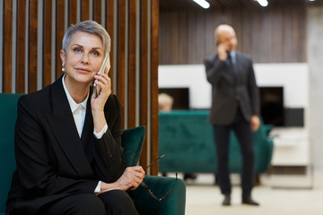 Wall Mural - Portrait of successful mature woman speaking by phone in modern office interior, copy space