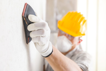 Plasterer or painter sanding a white wall