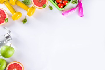 Fitness and healthy food lifestyle concept. Dumbbells, diet fruit and vegetable lunch box, water and jump rope on white background. Flatlay image, top view copy space