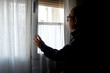 Un hombre mayor, confinado por la cuarentena del COVID-19, mira a través de la ventana de su casa