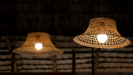 Focus on foreground of 2 vintage hanging lamps decoration with bamboo farmer's hat against straw thatched roof inside of traditional hut