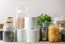 Food Supplies Crisis Food Stock For Quarantine Isolation Period. Different Glass Jars With Grains, Pasta, Cans Of Canned Food, Toilet Paper, Chalkboard Handwritten Chalk Lettering Stay Home And Relax.