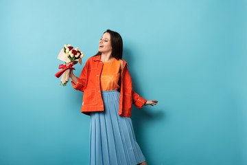 Wall Mural - shocked woman in jacket holding bouquet on blue background