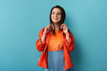 Wall Mural - smiling woman with headphones looking away on blue background