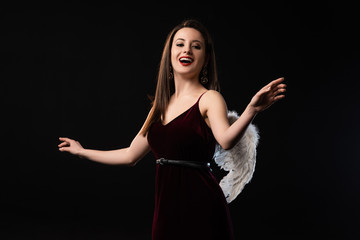 Wall Mural - shocked woman in dress with wings looking at camera isolated on black