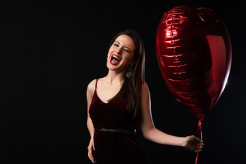 Wall Mural - happy woman in dress holding heart-shaped balloon and screaming isolated on black