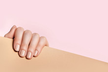 Female Hand Holds A Sheet Of Paper And Demonstrates A Nude Manicure. Pink, Beige Background With Place For Text.