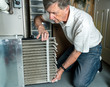 Senior caucasian man changing a folded dirty air filter in the HVAC furnace system in basement of home