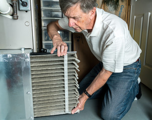 Wall Mural - Senior caucasian man changing a folded dirty air filter in the HVAC furnace system in basement of home