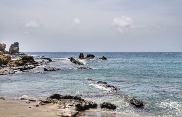 Wall Mural - Rock coastline with volcanic boulder aligning the beach