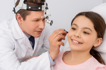 attentive ent physician examining ear of cute child with ear speculum