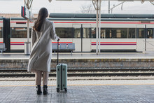 Back View Of Unrecognizable Female Traveler In Stylish Outfit Standing With Suitcase On Platform Of Railway Station