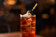 © Peter Karasev/ADDICTIVE STOCK - Highball glass with red alcohol cocktail with ice cubes decorated with stick with black olive on wooden counter