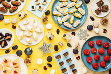 Top View Of Christmas Baubles And Snowflakes Placed Near Plates With Various Sweet Pastry On Yellow Background