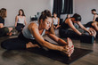 © JAKE JAKAB/ADDICTIVE STOCK - Diligent barefooted woman in sportswear performing head to knee forward bend exercise on mat while other sporty people resting after training in light contemporary gym
