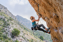 From Below Side View Of Active Focused Youthful Female Alpinist Climbing On Cliff In Summer Day