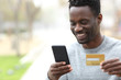 © PheelingsMedia - Happy black man paying online with credit card on phone