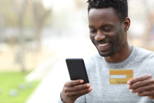 Happy Black Man Paying Online With Credit Card On Phone