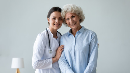 Wall Mural - Portrait of optimistic old lady pose look at camera with caring young woman doctor, smiling happy senior mature grandmother with nurse or caregiver in hospital or at home, elderly healthcare concept