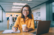 © BullRun - Portrait of happy Asian woman smiling at camera during studying process in university campus feeling excited from exam preparation, emotional female in trendy spectacles e learning in coffee shop